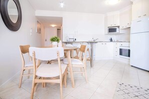 Cozinha moderna com armários brancos, micro-ondas e geladeira. Há uma área de jantar com mesa redonda e cadeiras de madeira.