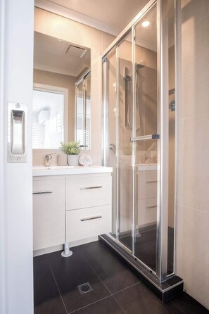 Ein modernes Badezimmer mit einer ein Glaswand-abgetrennten Dusche, einem weißen Waschtisch mit Spiegel und einer Topfpflanze.