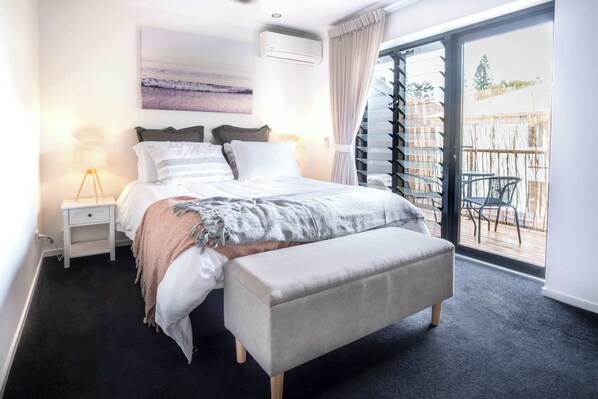 A bedroom with a bed, bedside table, bench, and a view through a sliding glass door to an outdoor area.