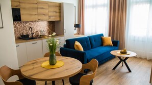 A modern living room with a blue sofa, wooden dining table, and chairs. - Miedziany (Torun)