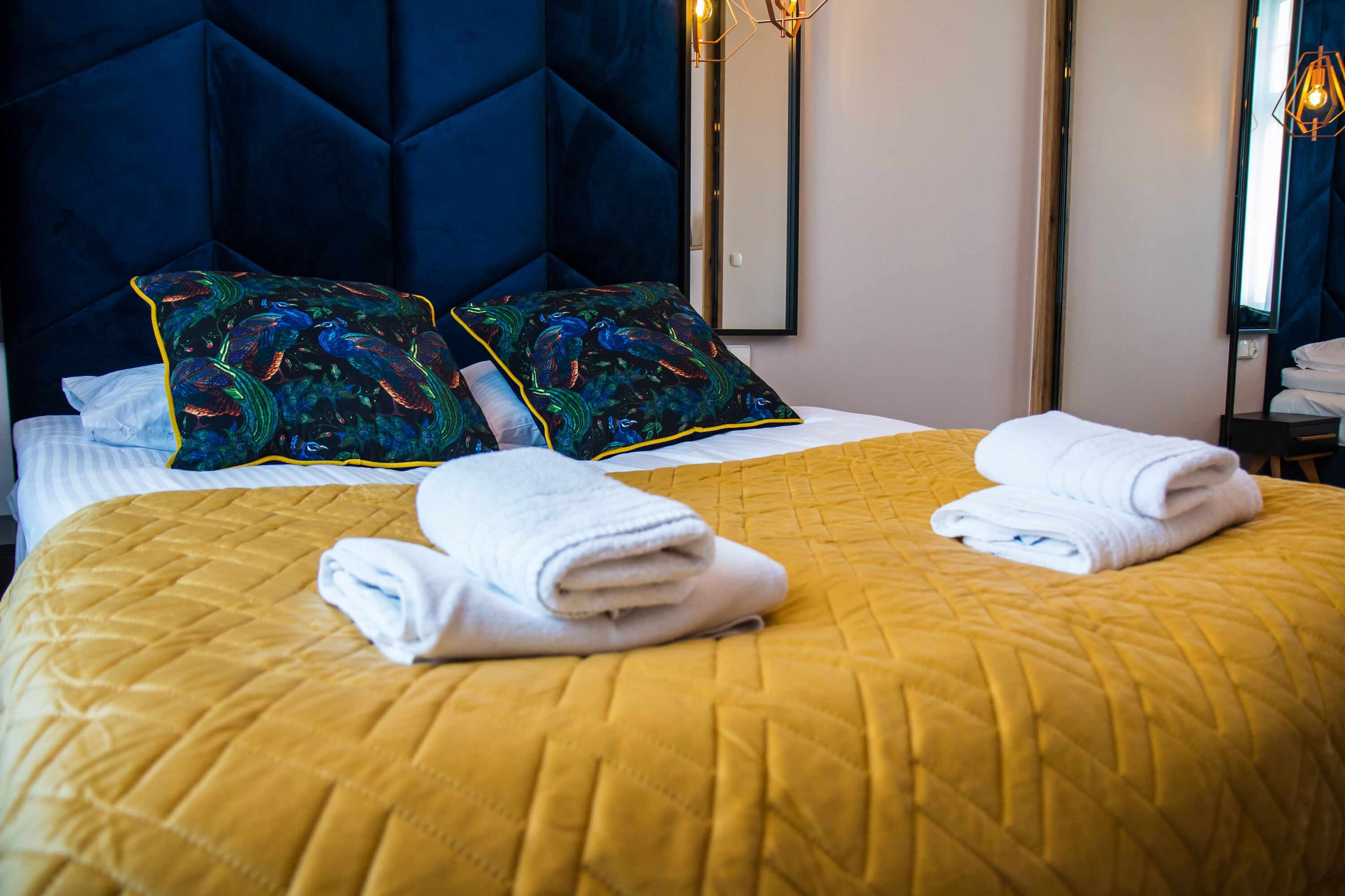 Habitació d'hotel amb un llit gran, un reposacapses blau i dos coixins decoratius.