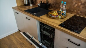 A modern kitchen with a wooden countertop, a black sink, a dishwasher, and an induction cooktop. - Miedziany (Torun)