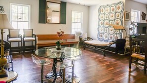 A living room with a glass table, chairs, a bench, a ceiling fan, and a quilted wall hanging.