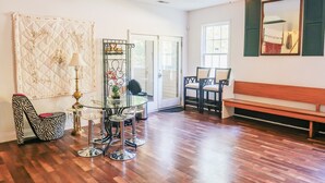 A spacious room with a wooden floor, a glass dining table, a zebra-patterned chair, a wooden bench, and a ceiling fan.