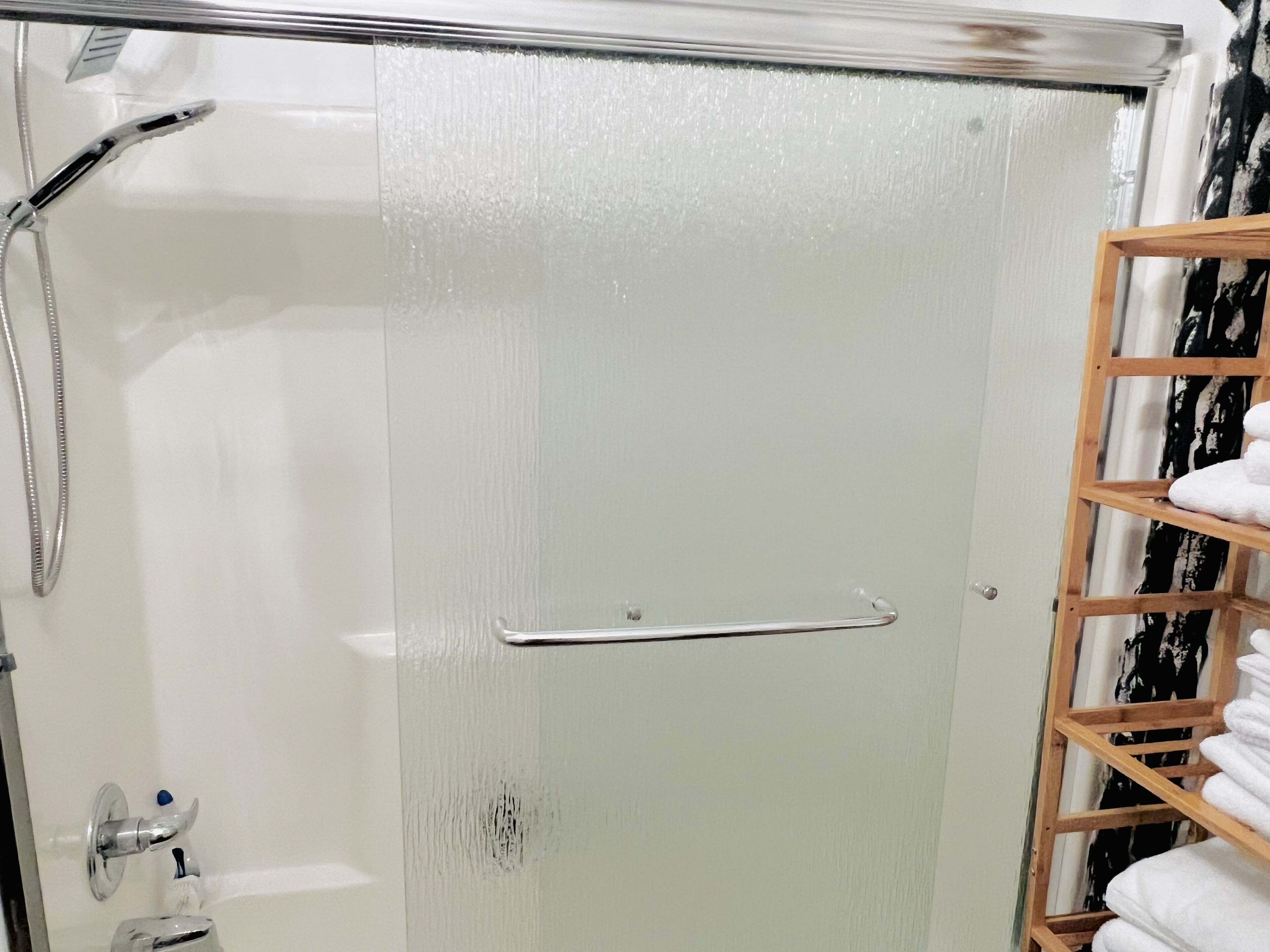 A bathroom with a glass shower door, a wooden towel rack, and a visible showerhead.