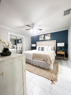 A bedroom with a bed, bedside tables, a ceiling fan, a mirror, and a dresser.