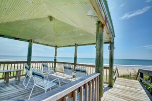 A wooden deck with a covered area, chairs, and a bench overlooking the beach.