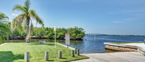A waterfront park with a concrete walkway, palm trees, and a warning sign about no parking.