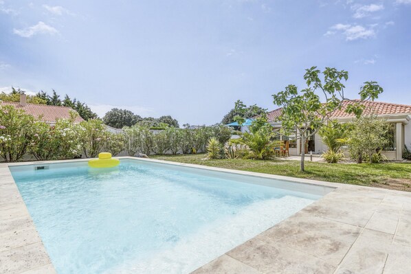 A rectangular swimming pool with a yellow float in the center, surrounded by a well-maintained garden with various plants and trees.