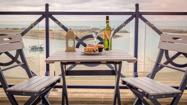 A balcony with two wooden chairs, a small table, and a bottle of wine. - Seaviews Sovereign Harbour - adults-only apartment with stunning water views (Eastbourne)