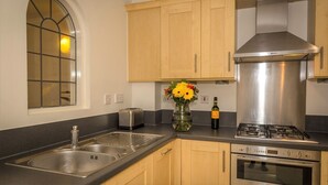A kitchen with wooden cabinets, a stainless steel sink, a toaster, a vase with flowers, a bottle of wine, and a gas stove. - Seaviews Sovereign Harbour - adults-only apartment with stunning water views (Eastbourne)