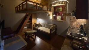 A cozy interior with a wooden staircase, a sofa, a small table, and a kitchen area with a sink and countertop. - An ambient 19th century semi-basement studio only steps from the Cretan Sea (Χανιά)