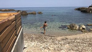 A wooden deck overlooking a rocky beach with clear water and distant swimmers. - An ambient 19th century semi-basement studio only steps from the Cretan Sea (Χανιά)