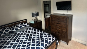 Un dormitorio con cama, cómoda, mesita de noche, ventilador de techo, televisor y espejo.