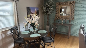 Un comedor con una mesa redonda, sillas, un jarrón con flores, un espejo enmarco y una planta en maceta.