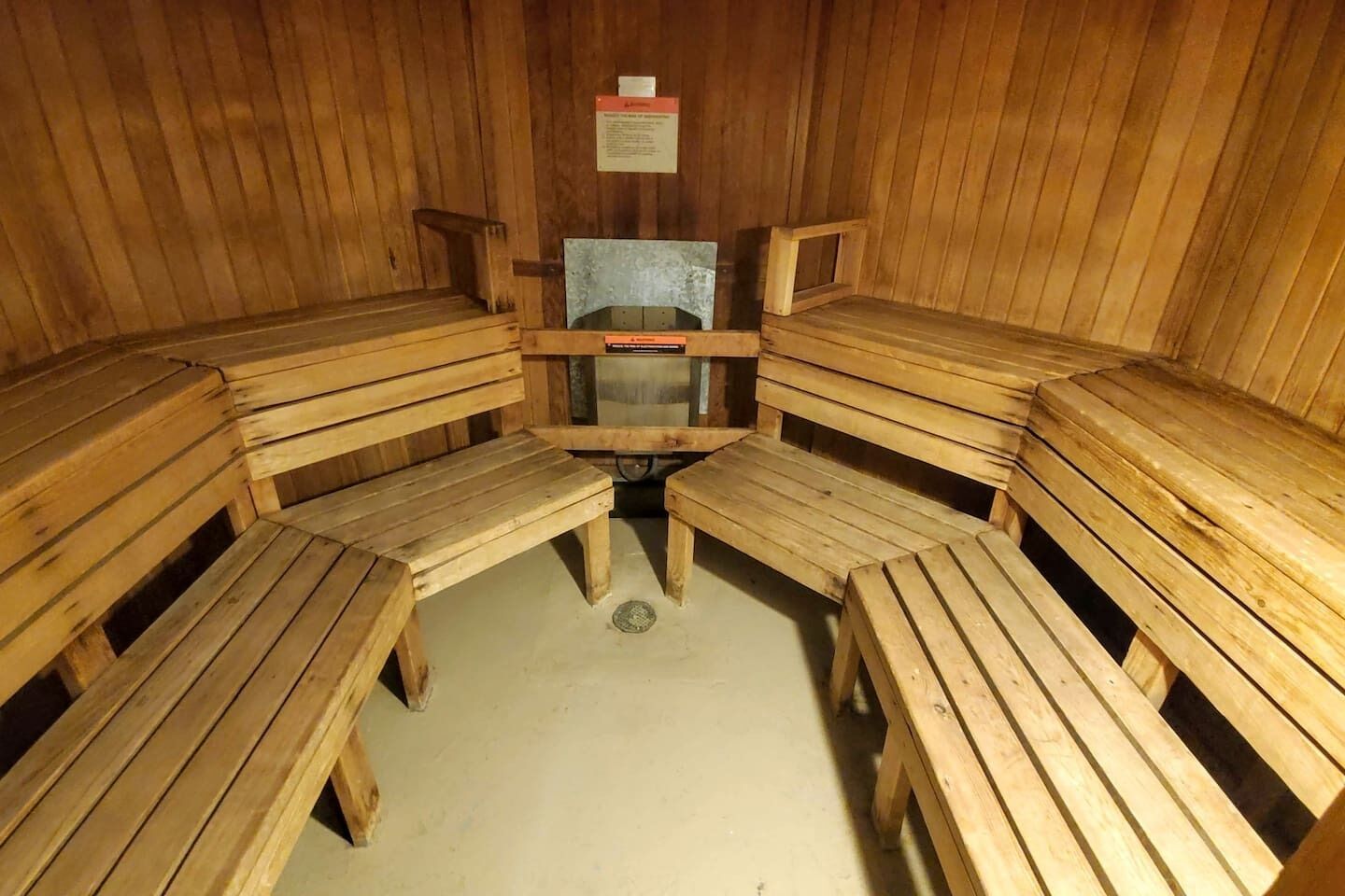 Un sauna avec des bancs en bois disposés en demi-cercle, un banc central et un panneau sur le mur.