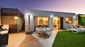 A modern house with a dining area, outdoor seating, and a staircase leading to an upper level.