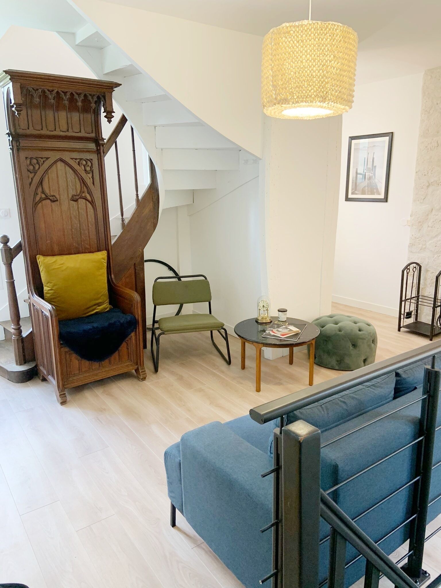 Un salon moderne avec un escalier, un canapé bleu, un fauteuil vert et une chaise en bois avec un coussin jaune.