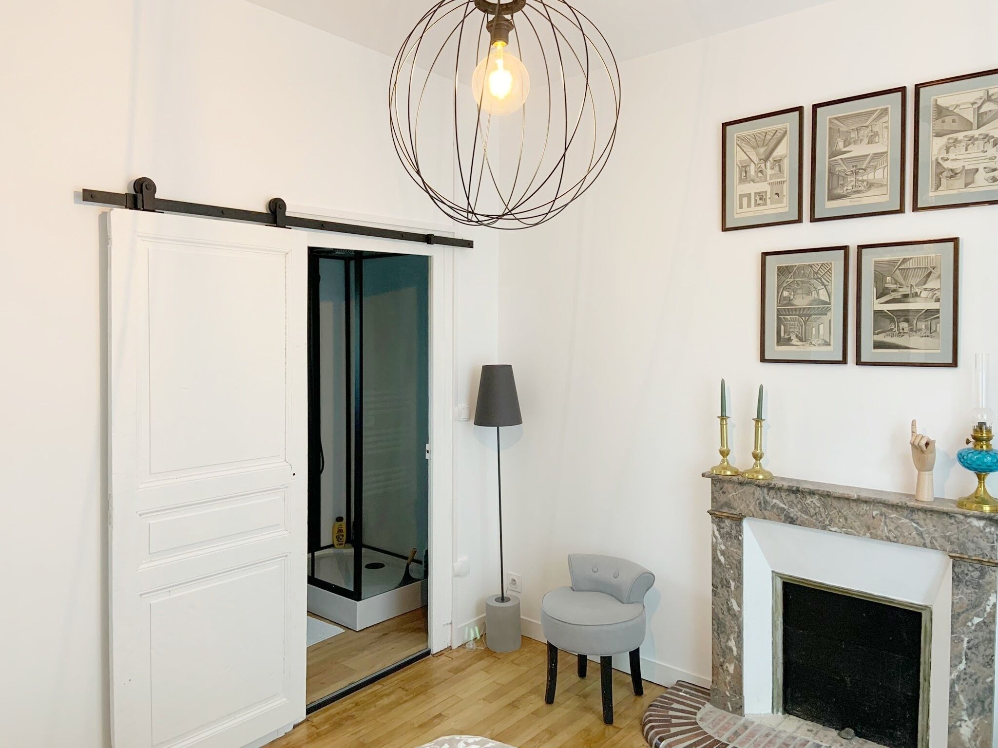 Un salon moderne doté d’une porte coulissante donnant accès à une salle de bain, d’une cheminée et de reproductions d’architectures encadrées accrochées au mur.