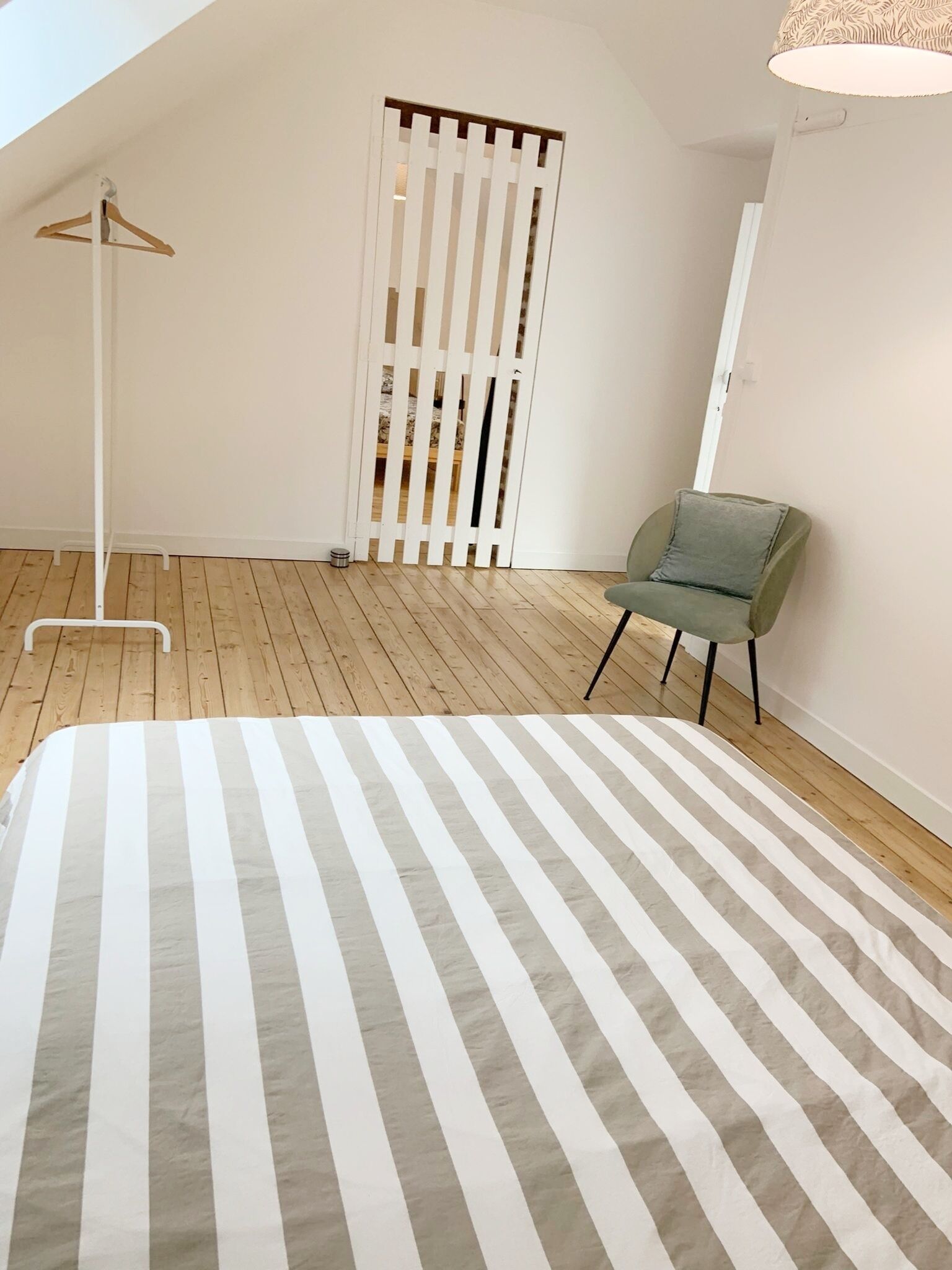Een slaapkamer met een gestreept bedovertrek, een groene stoel, een witte kledingkast en een houten vloer.