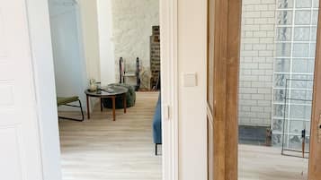 Une porte ouverte donne sur un salon avec un mur en pierre, un canapé bleu et un meuble en bois doté d’une porte vitrée.
