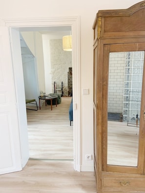 Une porte ouverte donne sur un salon avec un mur en pierre, un canapé bleu et un meuble en bois doté d’une porte vitrée.