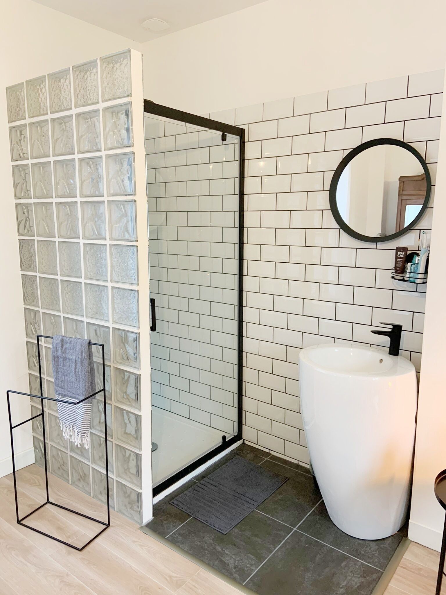 A bathroom with a glass shower enclosure, a white sink, and a tiled wall.