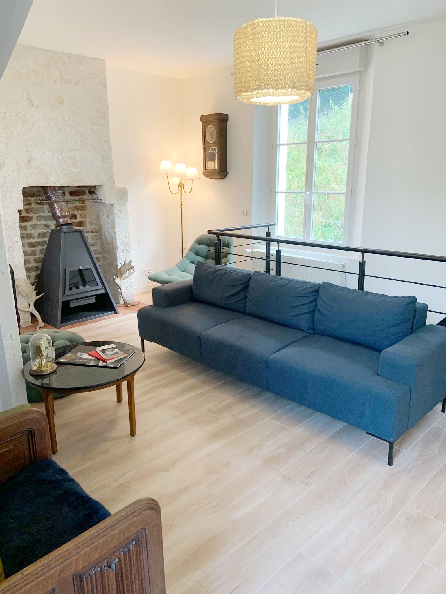 A modern living room with a stone fireplace, a blue sofa, a round coffee table, and a hanging light fixture.
