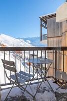 Un balcón con sillas y una mesa de metal, con vista a un paisaje montañoso nevado.