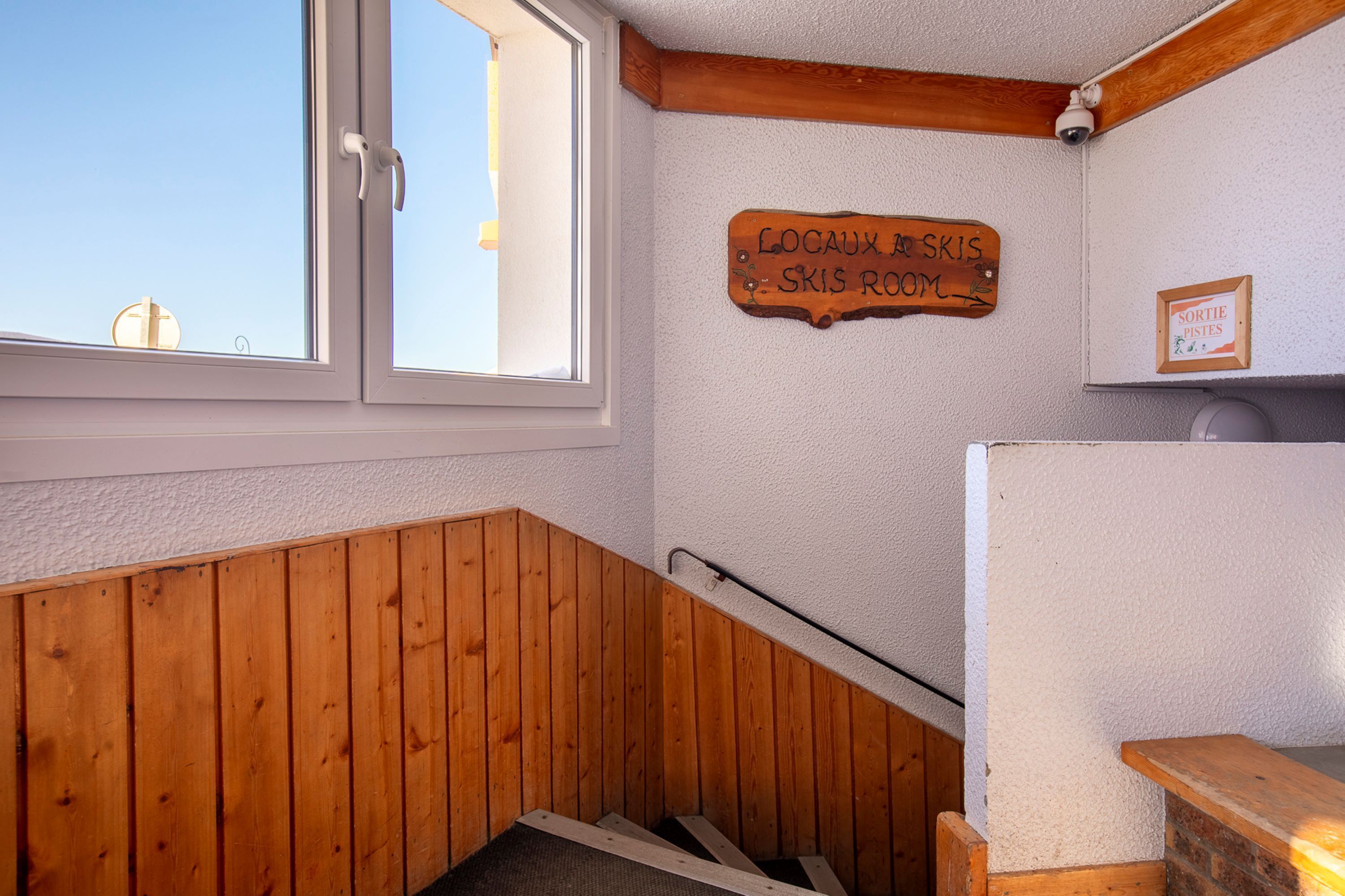 Una scala in legno con corrimano in legno e un cartello che indica 'Locaux à skis' e 'Skis room'.