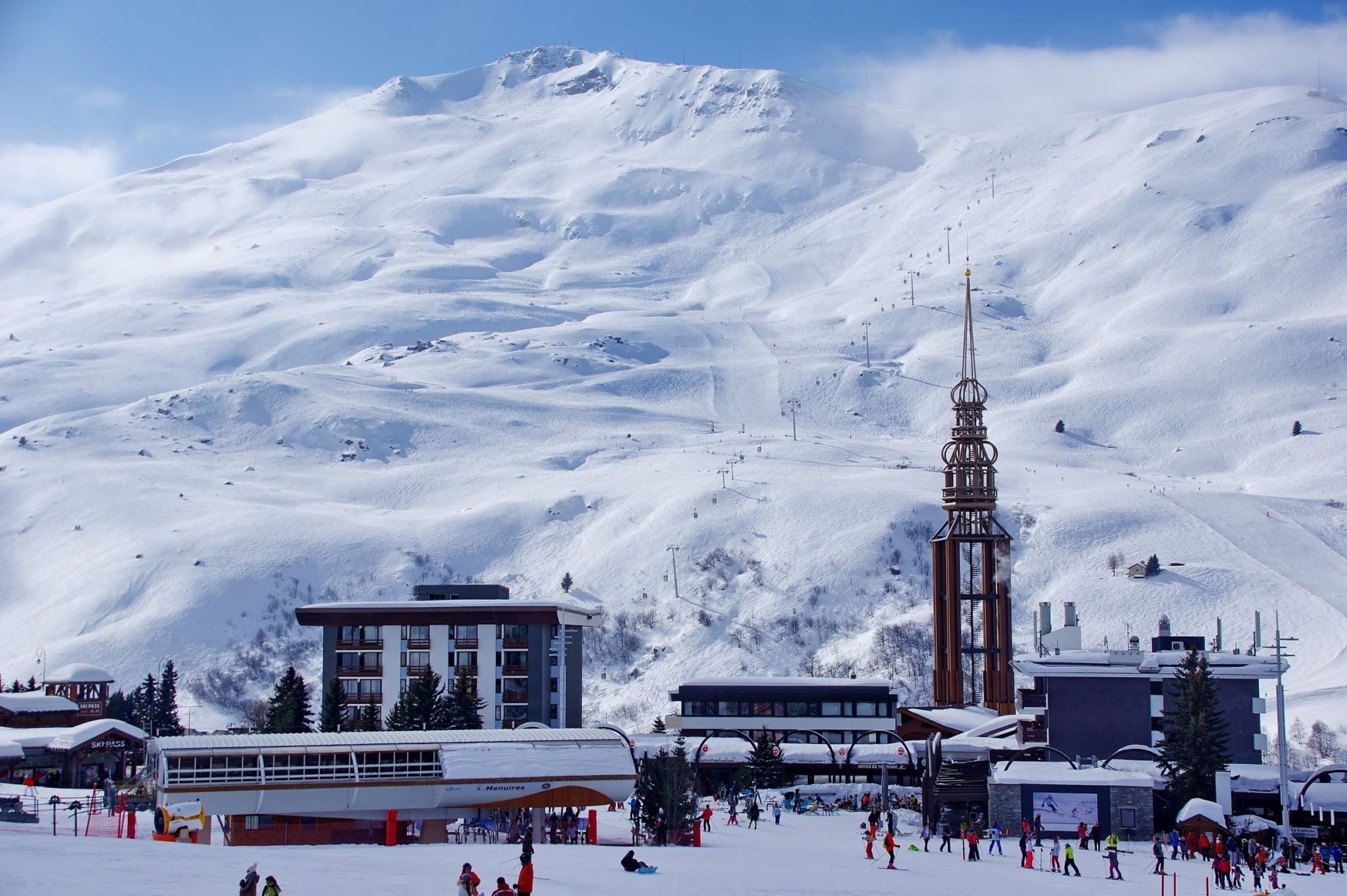 A snow-covered ski resort with a prominent ski lift tower, buildings, and a bus for transportation.