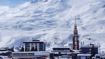 A snow-covered ski resort with a prominent ski lift tower, buildings, and a bus for transportation.