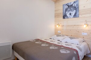 Un dormitorio con pared de madera, una cama con ropa de cama estampada y un cuadro de lobo sobre la cama.