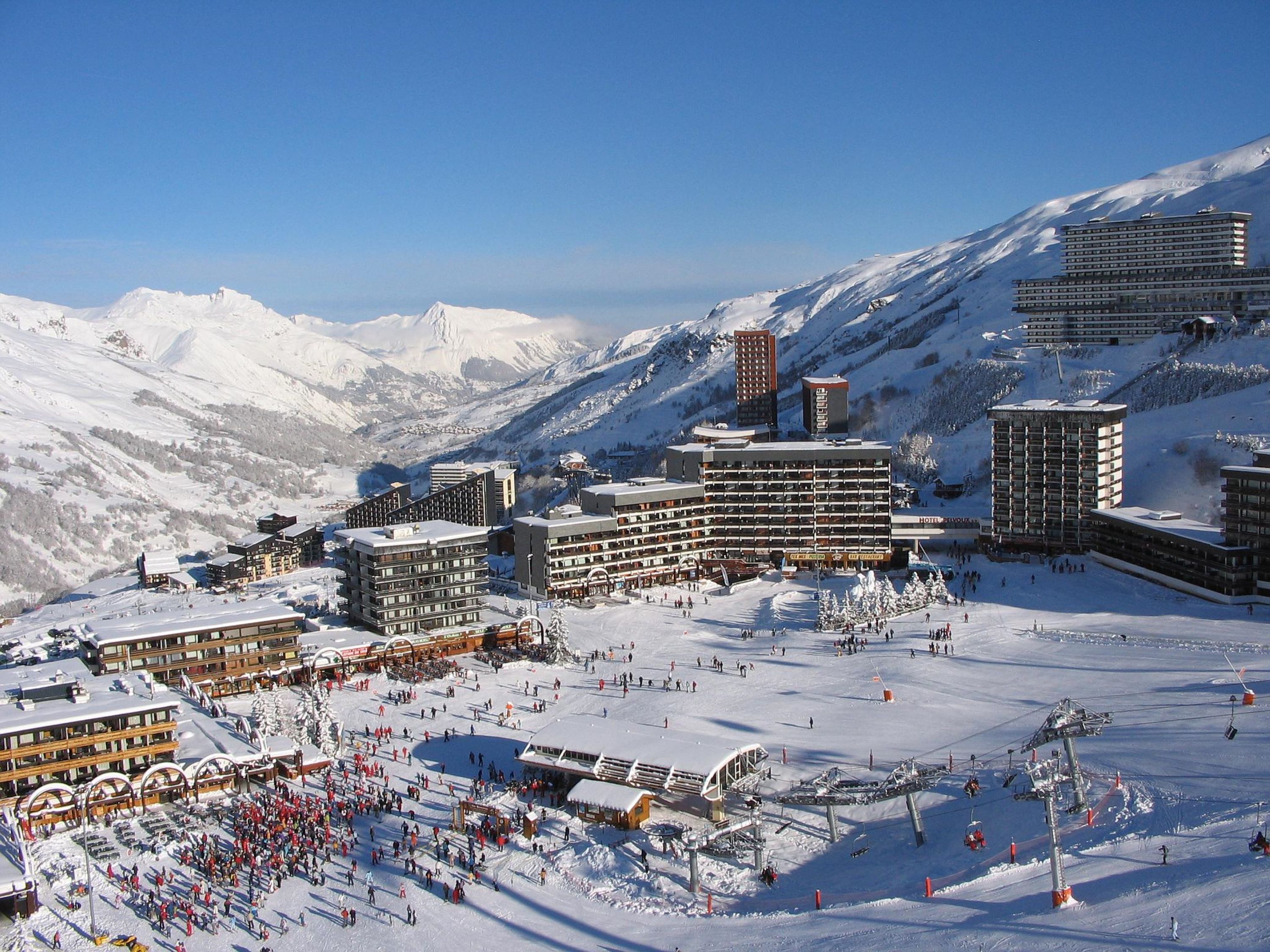 A snow-covered ski resort with multiple buildings, including a hotel with balconies and a ski lift area.