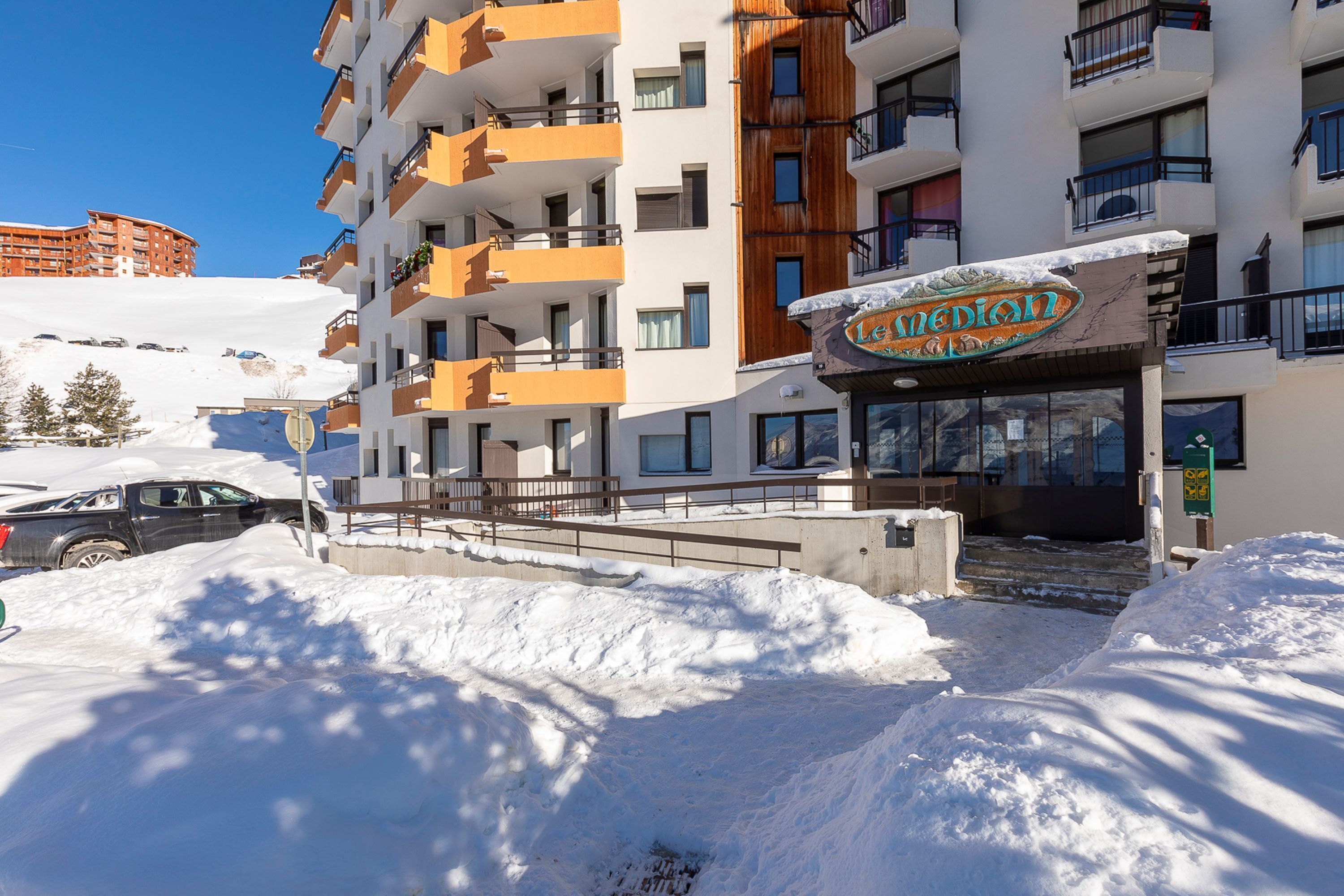 A hotel with multiple balconies, a snow-covered entrance, and a clear blue sky.