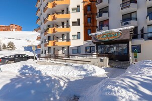Un hôtel doté de nombreux balcons, d’une entrée enneigée et surplombant un ciel d’un bleu limpide.