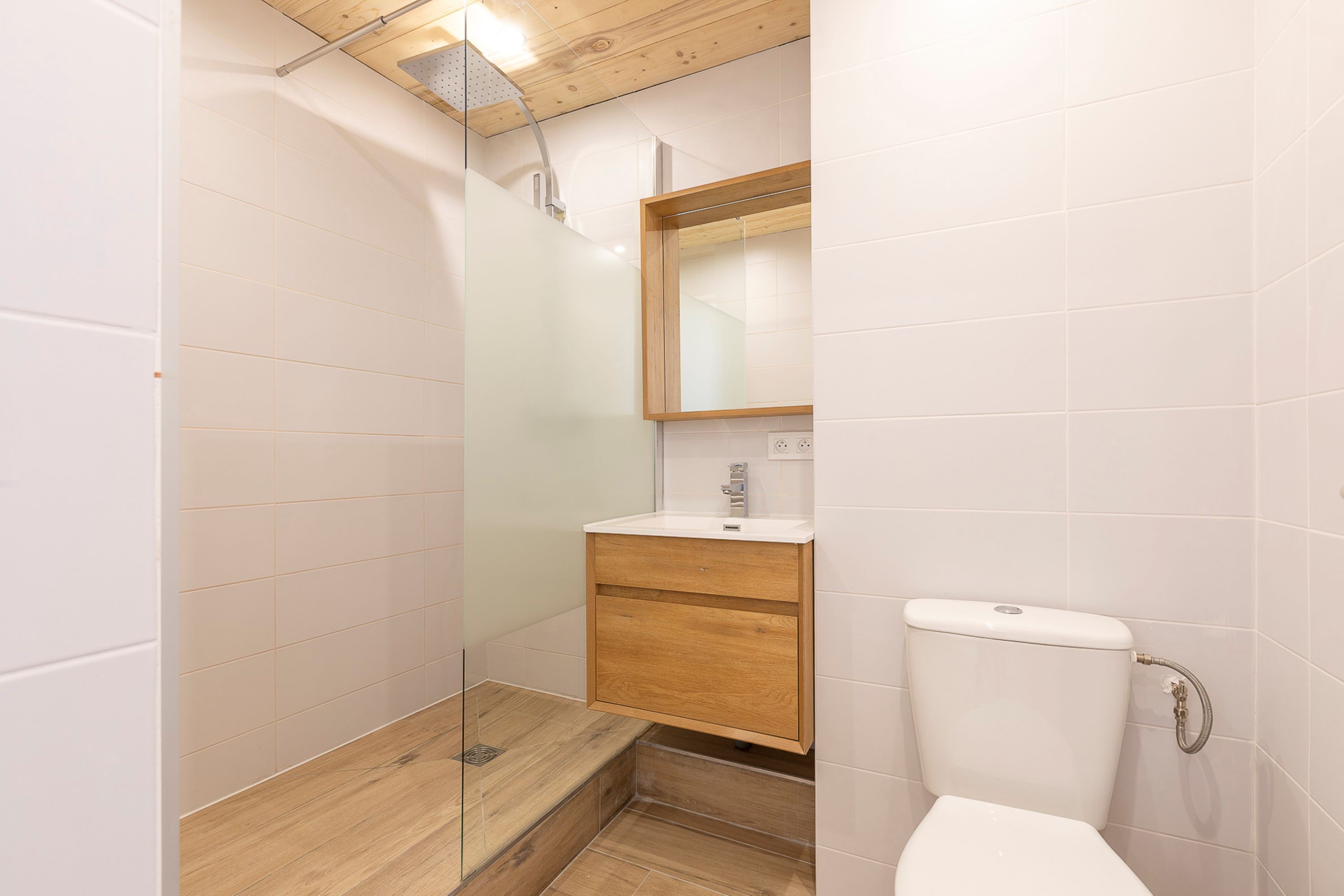 Een moderne badkamer met een douchecabine van glas, een houten wastafelmeubel en een wit toilet.