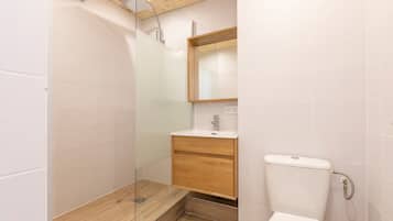 Een moderne badkamer met een douchecabine van glas, een houten wastafelmeubel en een wit toilet.