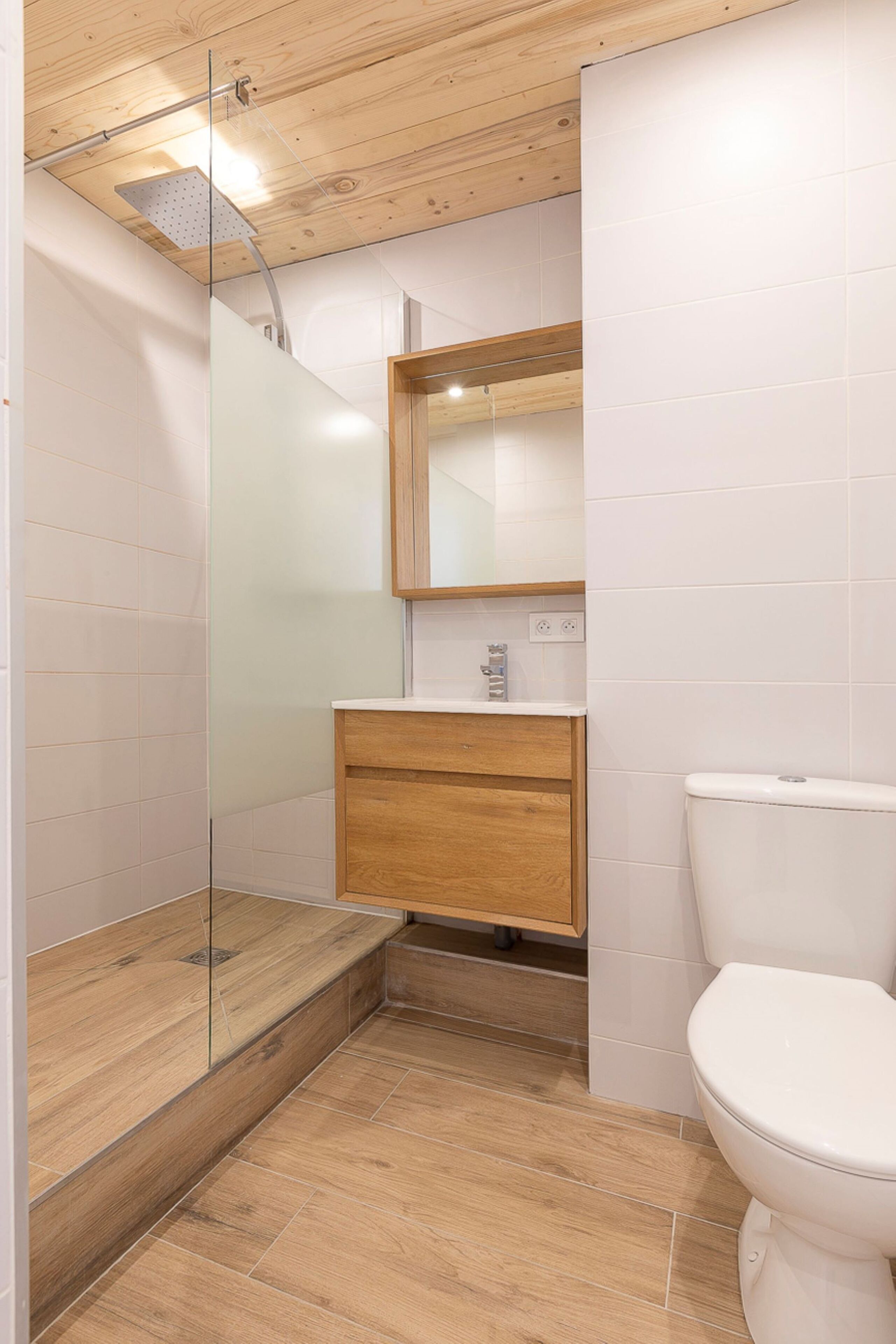 A modern bathroom with a glass shower enclosure, a wooden vanity, and a white toilet.