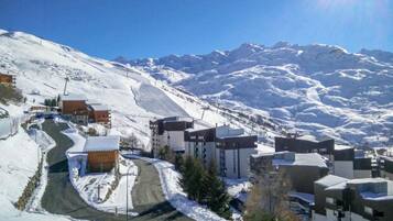 Un village de montagne enneigé, avec des bâtiments modernes, une route sinueuse et un ciel bleu dégagé.