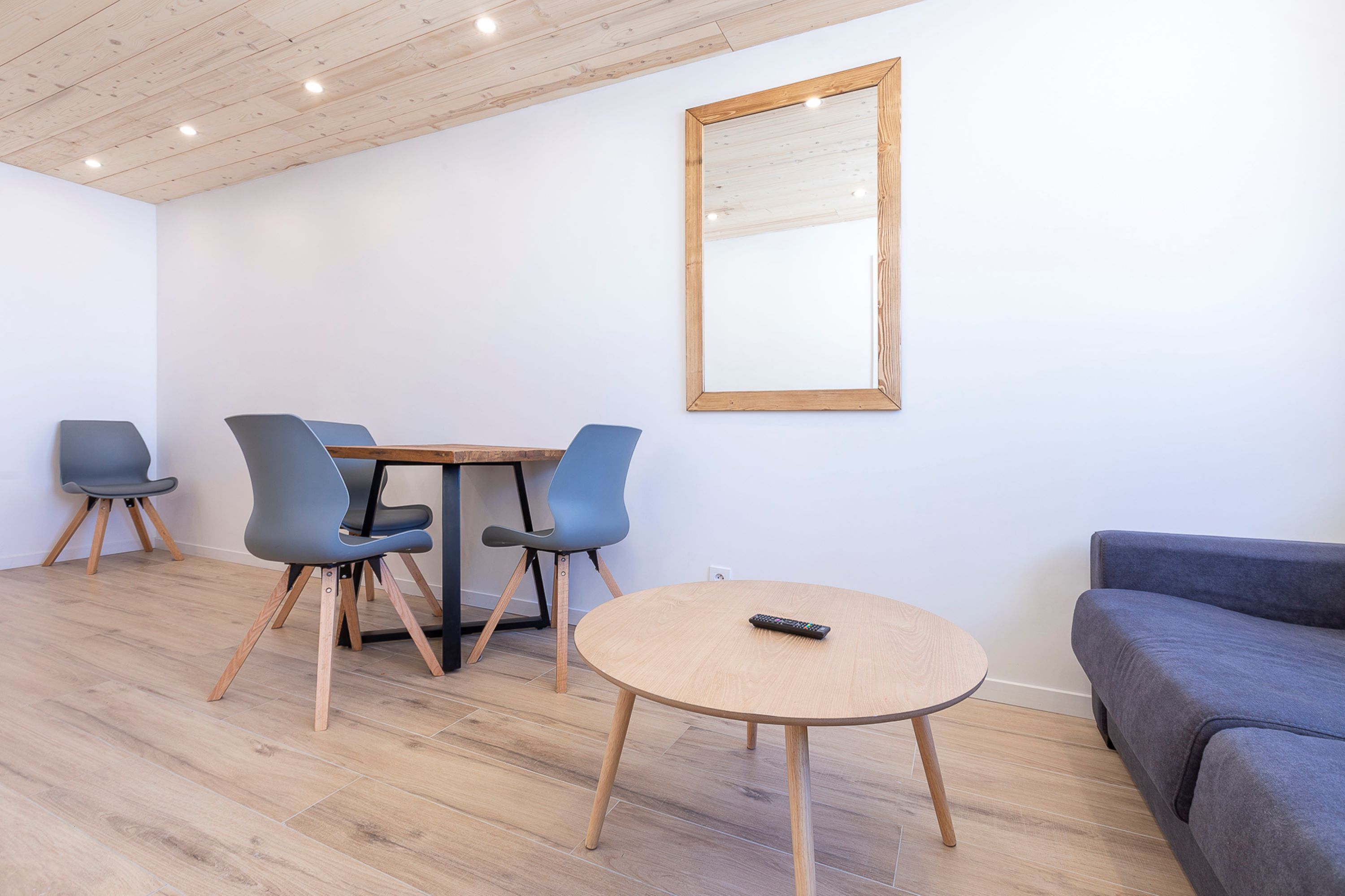 Una habitación moderna con techo de madera, una mesa redonda con sillas, un sofá y un espejo en la pared.