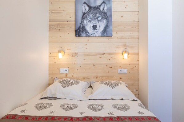 Un lit avec une couvre-lit à motifs, deux oreillers et un tableau représentant un loup, accroché au mur.