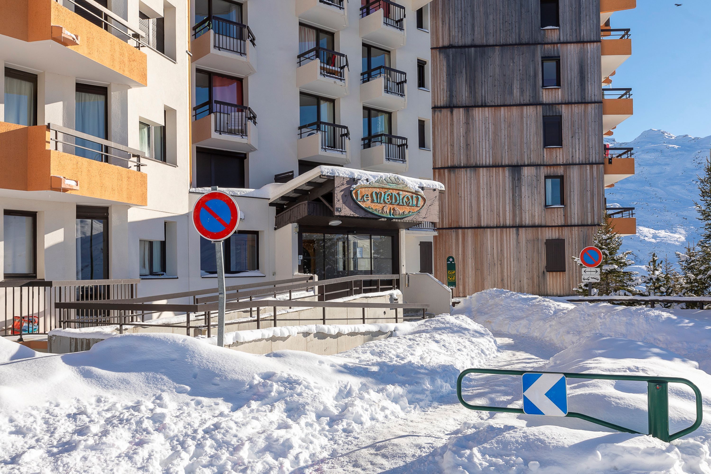 A hotel with balconies, a sign reading "Le Median," and a snow-covered landscape with mountains in the background.