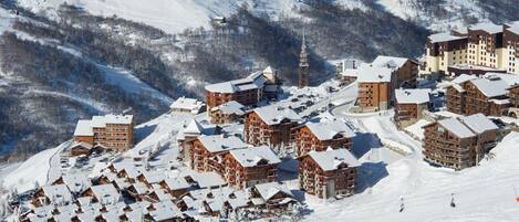 A snow-covered ski resort with multiple lodge buildings, ski slopes, and a ski lift.