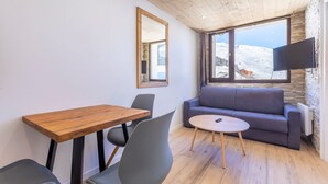 Een moderne woonkamer met een houten tafel, grijze stoelen, een grijze bank en een televisie die aan een stenen muur is bevestigd.