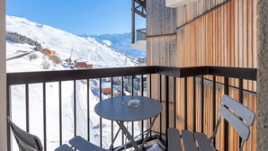 Een balkon met een tafel en stoelen, met uitzicht op een besneeuwd berglandschap.