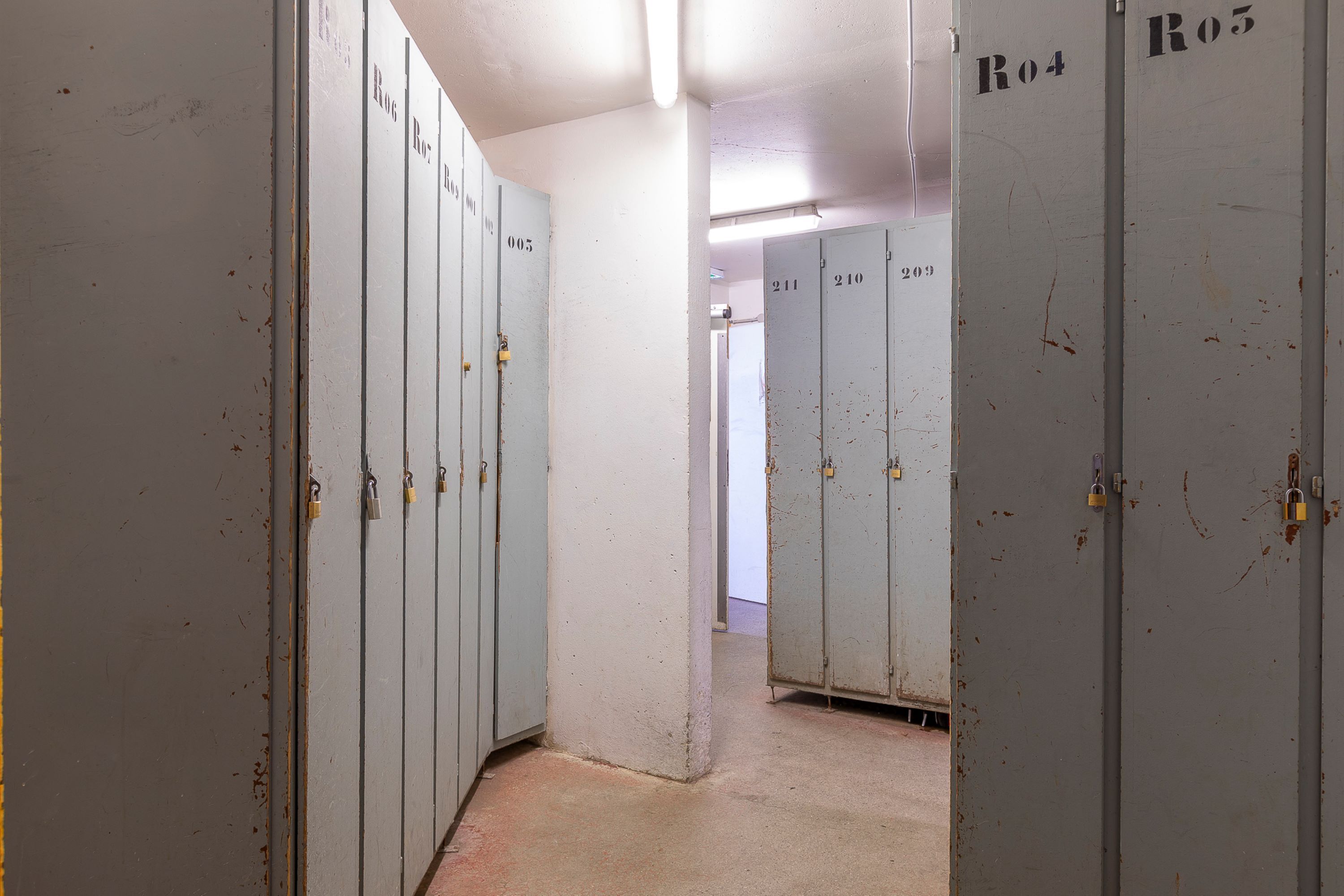 A corridor with lockers numbered R04 to R05, leading to a door with the number 211.