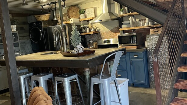 Una cucina con isola centrale, sgabelli da bar, una scala e un'area pranzo con divano.