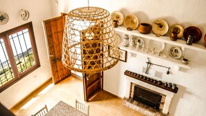 Una cocina con una mesa de comedor, sillas, una lámpara colgante y un estante con vajilla.