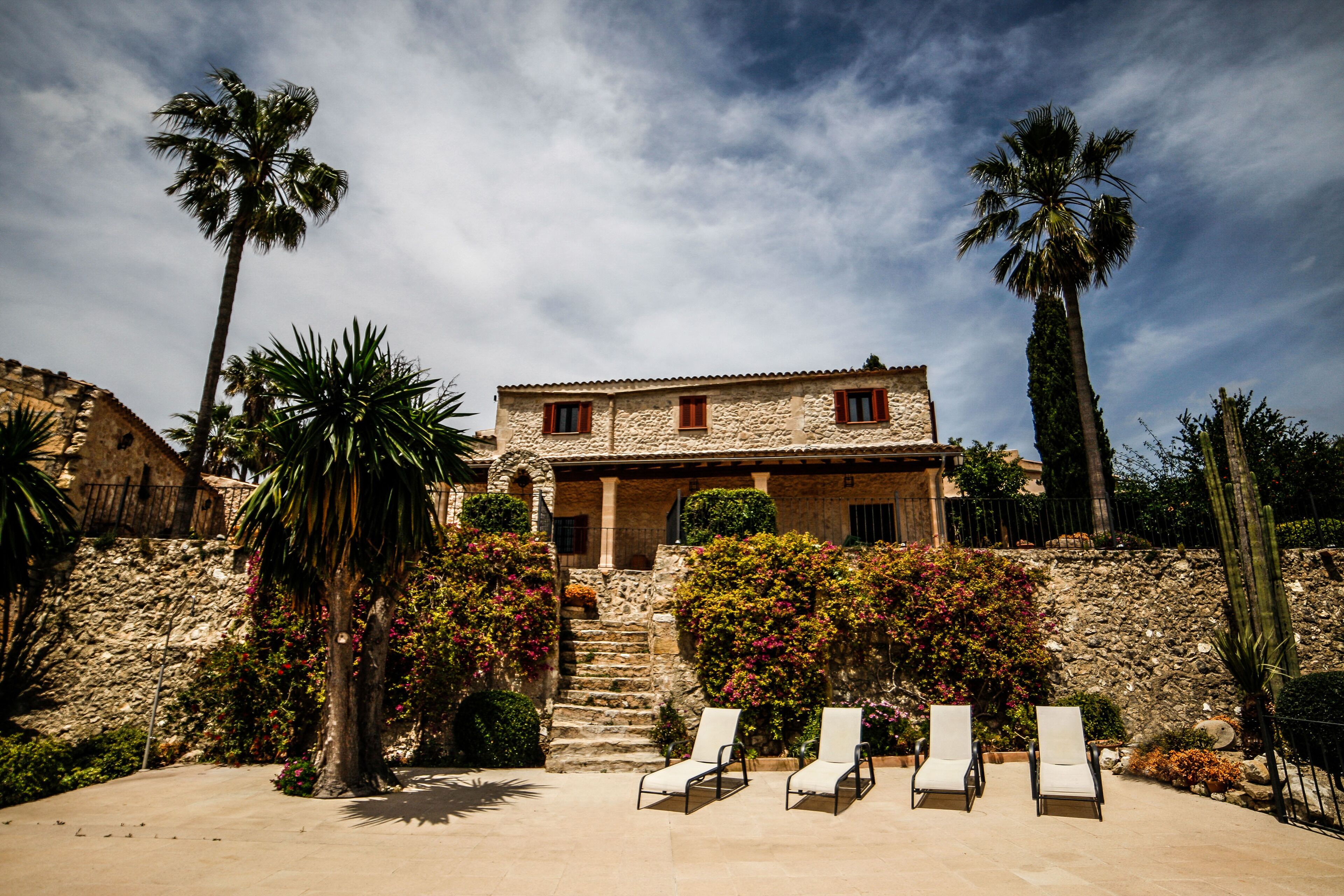 A stone house with a terrace, palm trees, and a stone wall.